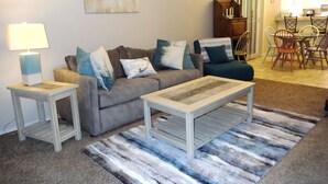 A living room with a sofa, two side tables, a coffee table, and a striped rug. - 2 BR 2 bath -  pool - 3 minute walk to beach! (Corpus Christi)