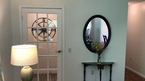 A room with a white door, a round mirror, a small table with a vase of flowers, and a lamp on a round table. - New photos with many updates! Bring your EV cord and adapter!  Walk to the fun! (Stonington)