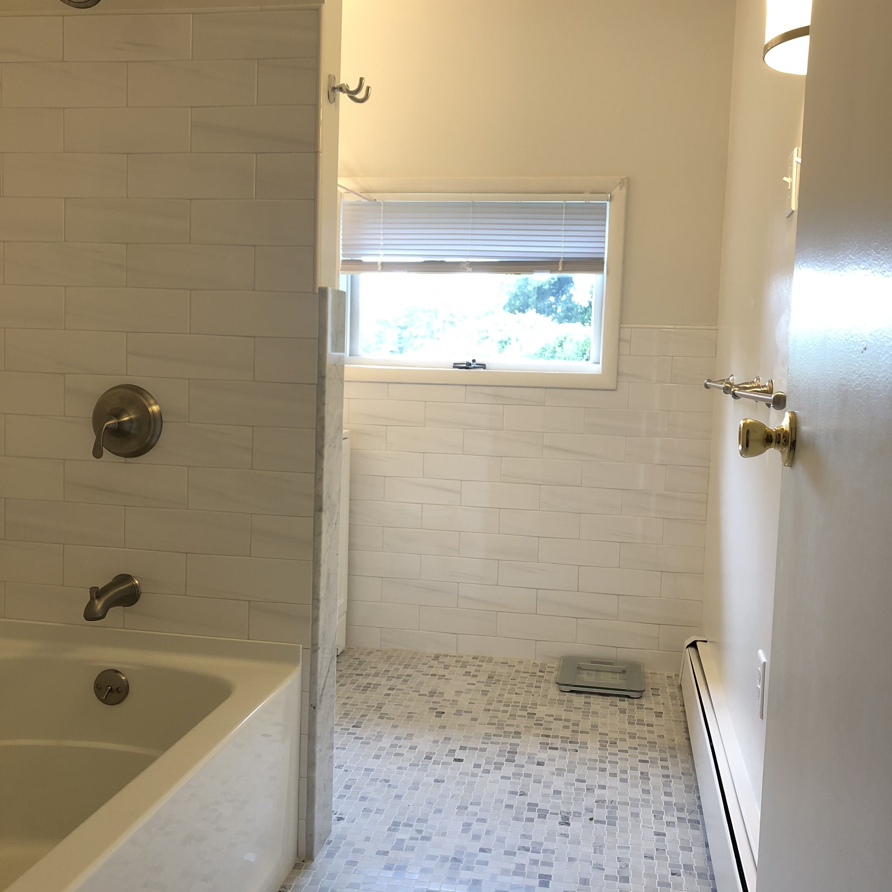 Un baño con bañera, una ventana con persianas y piso de baldosas.