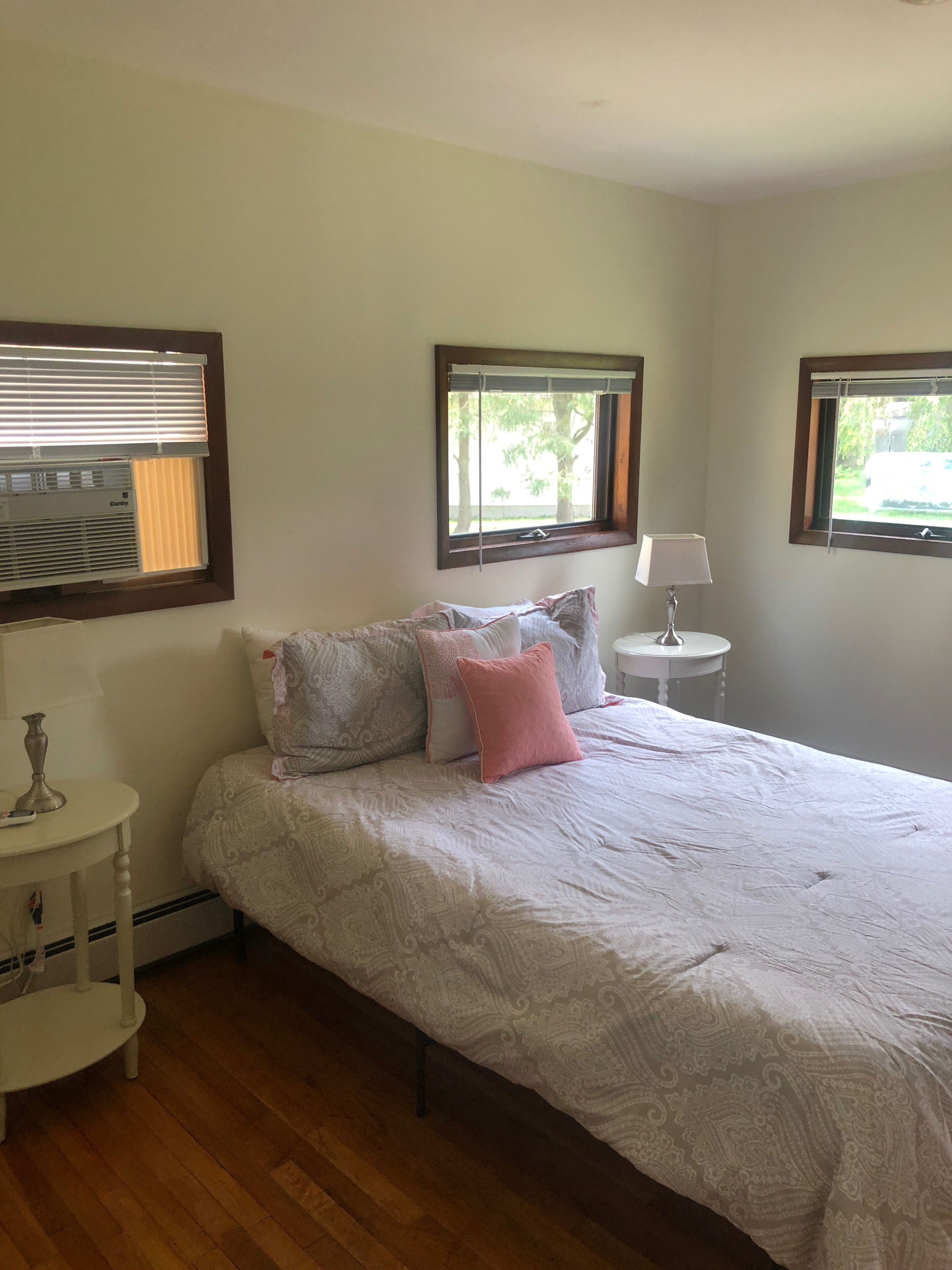 Une chambre à coucher comprenant un lit, deux tables de chevet, une lampe et trois fenêtres équipées de stores.
