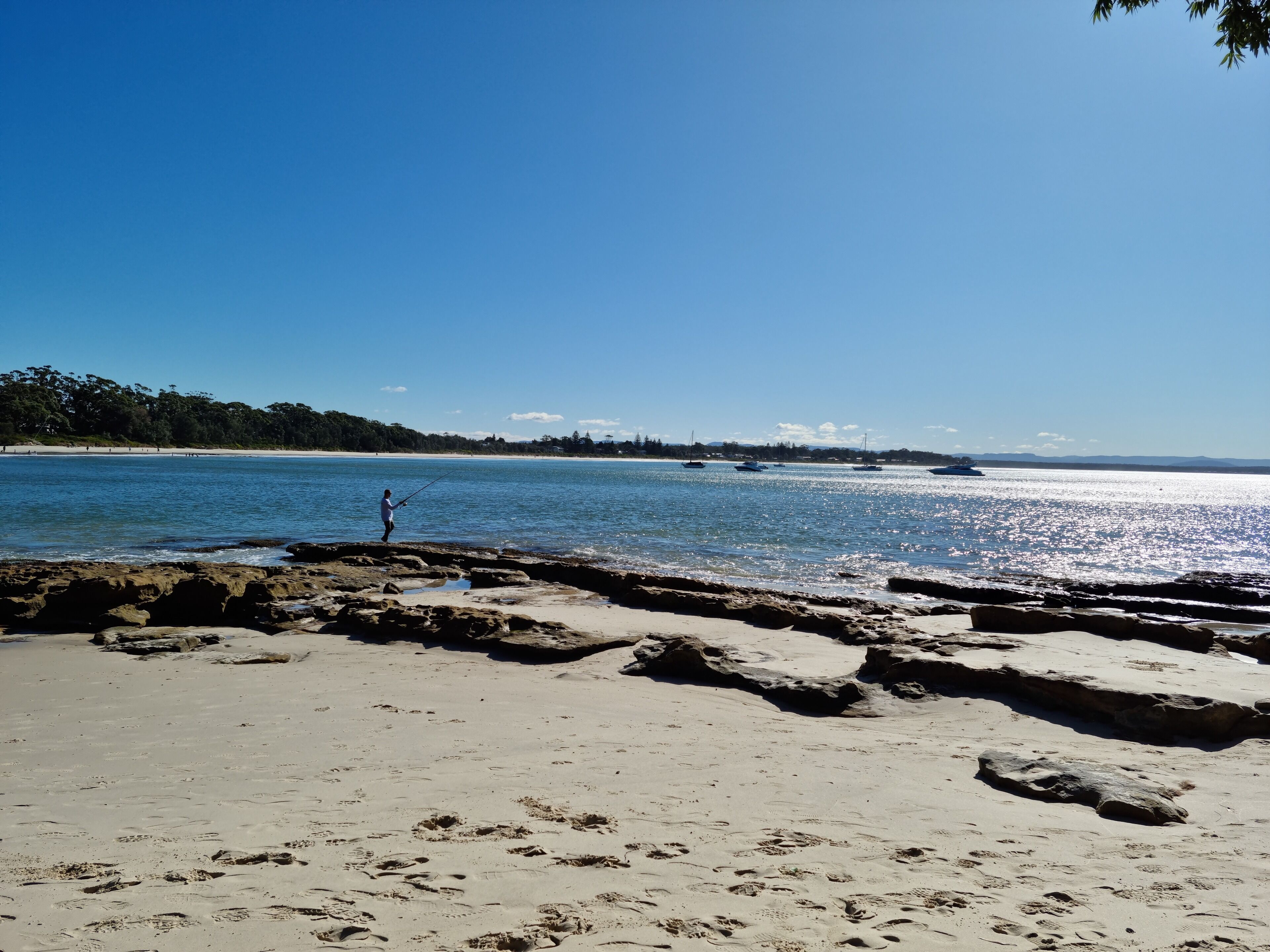 Une plage à l’eau claire, avec des bateaux et une côte rocheuse.