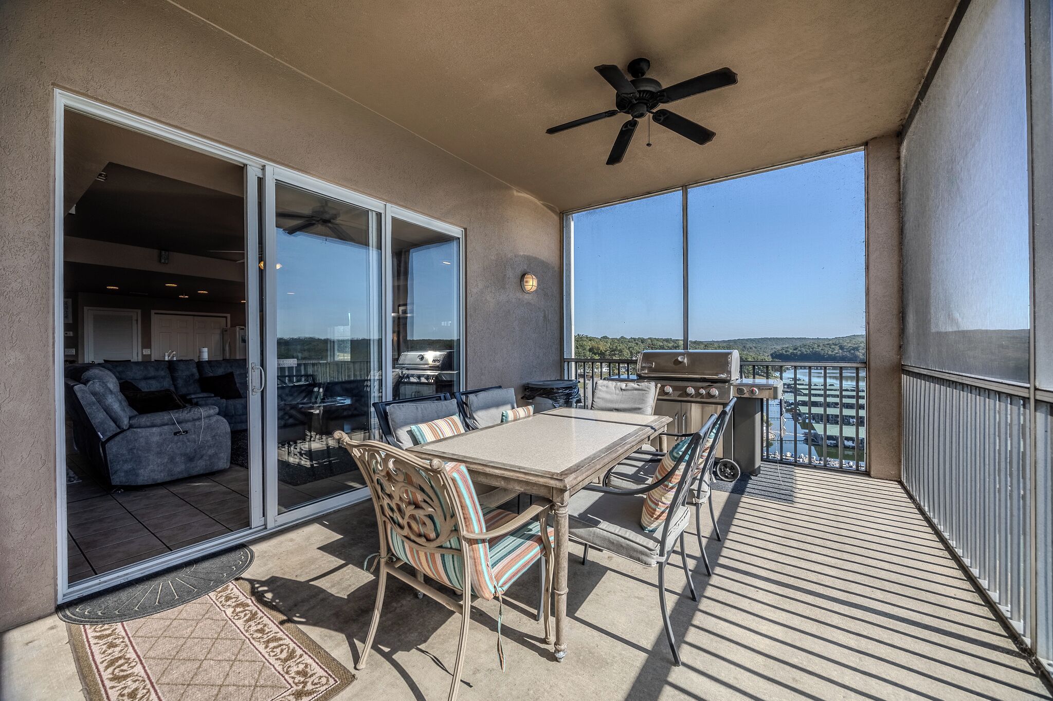 A balcony with a table and chairs, a grill, and a view of the water.