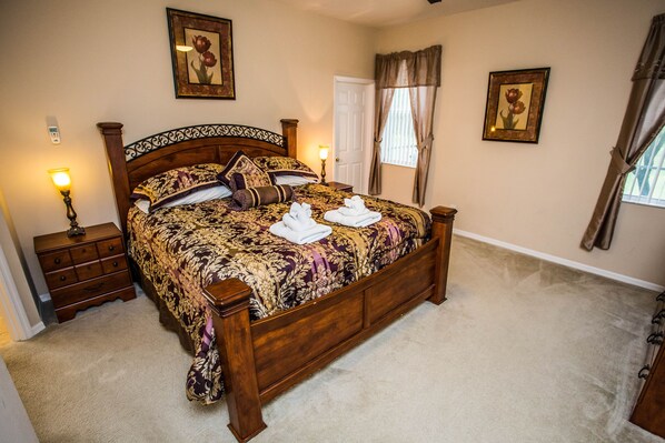 A neatly made bed with a floral bedspread, a bedside table with a lamp, and a door with curtains.