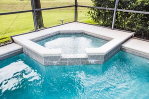 A rectangular hot tub with a tiled edge, surrounded by a glass enclosure, set in a pool.