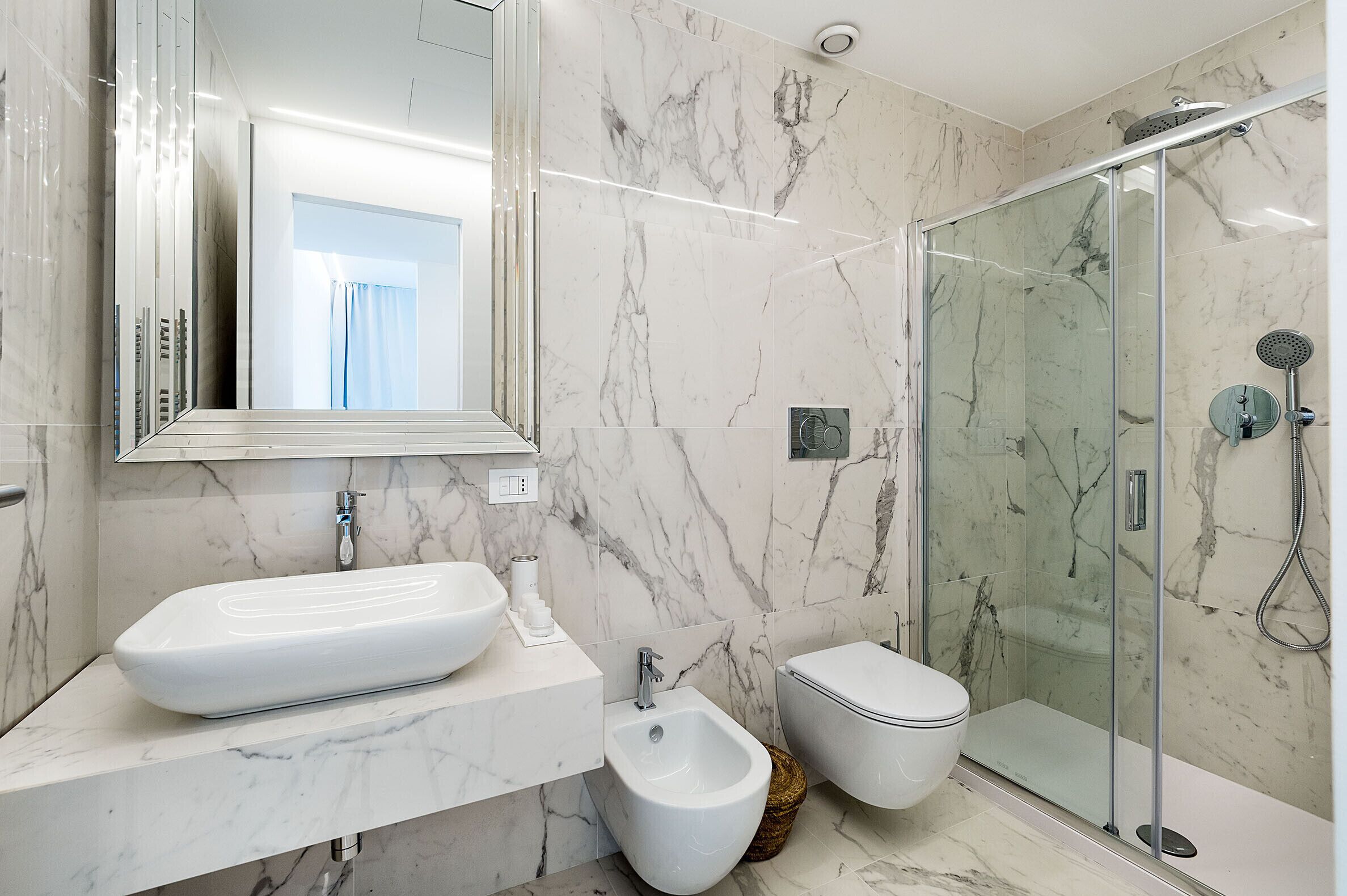 A modern bathroom with a large marble sink, bidet, and glass-enclosed shower.