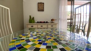 Una habitación con suelo de baldosas, una silla blanca, un armario blanco con cajones y una ventana con vistas al exterior.