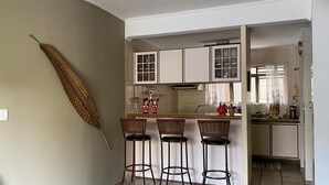 Una cocina con gabinetes blancos, una isla central con taburetes y una planta seca decorativa en la pared.
