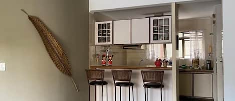 A kitchen with white cabinets, a central island with stools, and a decorative dried plant on the wall.