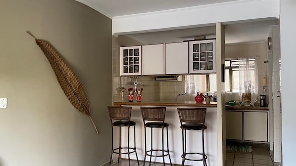 A kitchen with white cabinets, a central island with stools, and a decorative dried plant on the wall.