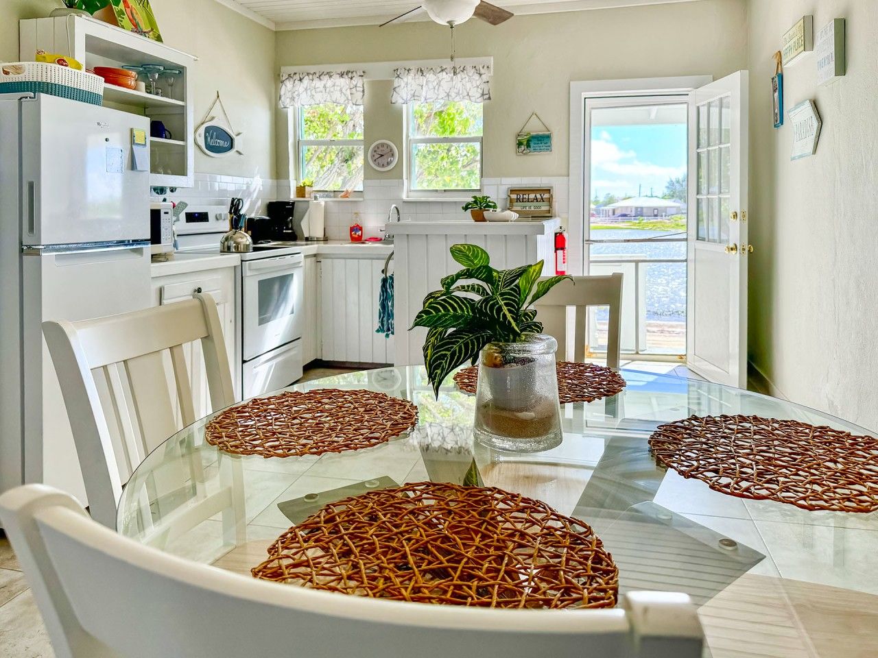 A dining area with a glass table, wicker placemats, and a potted plant.