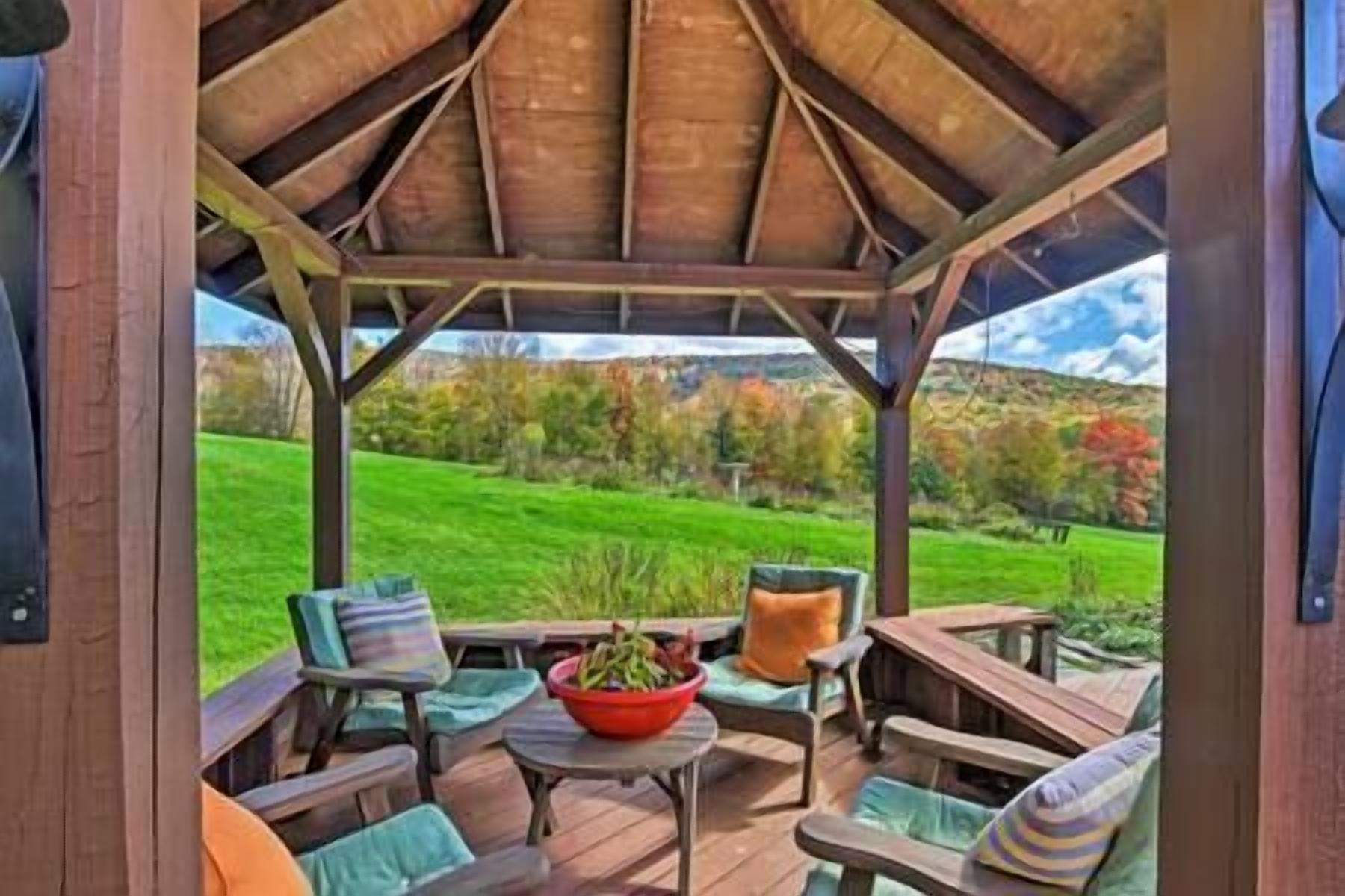 A covered outdoor seating area with wooden furniture and a view of a green landscape.