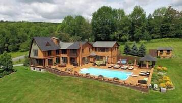 A large wooden house with a swimming pool, surrounded by a well-maintained lawn and trees.