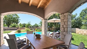Un patio al aire libre con una mesa de madera y sillas de mimbre, un pilar de piedra y vistas a una piscina.