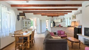 Amplia sala de estar con una mesa de comedor de madera, un sofá y un televisor. Se observa un área de cocina con una pared de piedra y una chimenea.