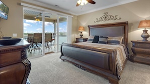 A bedroom with a large bed, a ceiling fan, a view through the glass door, and a dining area with chairs. - Lands' End V.I.P. 3 Suite Condo - Near Outlet Mall - Elevator, Wi-Fi, Water Park (Osage Beach)