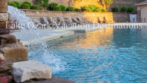 A swimming pool with a stone wall and a water feature in the foreground. - Lands' End V.I.P. 3 Suite Condo - Near Outlet Mall - Elevator, Wi-Fi, Water Park (Osage Beach)