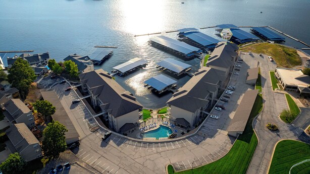 An aerial view of a waterfront property with a swimming pool, parking area, and several buildings with flat roofs. - Lands' End V.I.P. 3 Suite Condo - Near Outlet Mall - Elevator, Wi-Fi, Water Park (Osage Beach)
