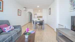 A modern living room with a grey sofa, a wooden coffee table, and a dining area with a white table and chairs. - 0086-BLAUCEL Apartment with seaview (Empuriabrava)