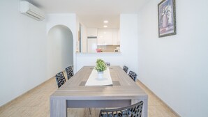 A dining area with a rectangular table, six chairs, a potted plant, and a kitchen in the background. - 0086-BLAUCEL Apartment with seaview (Empuriabrava)