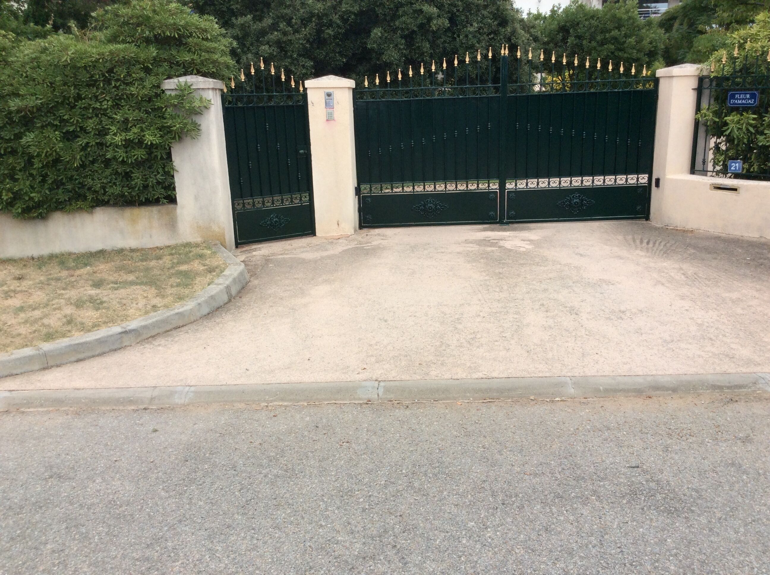 Une entrée fermée par un portail, avec un chemin en béton menant à un bâtiment.