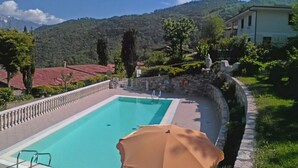 Piscina rectangular con muro de piedra y barandilla, rodeada de follaje y vistas a montañas.