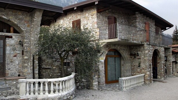 Un edificio de piedra con ventanas y puertas de arco, un balcón y un patio de grava.