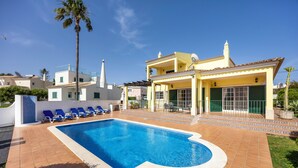 A swimming pool with blue water, surrounded by a tiled deck and blue lounge chairs.