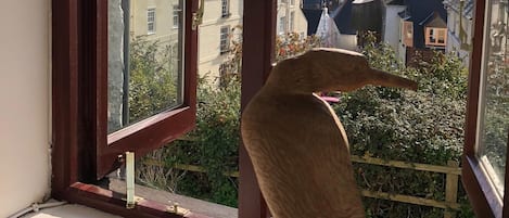 A window with a view of a town, a wooden sculpture on the windowsill, and a clear sky.