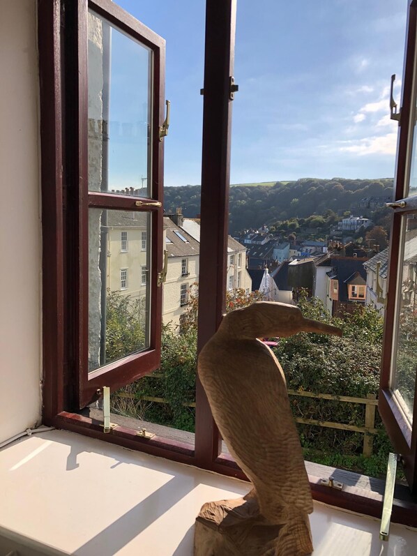 A window with a view of a town, a wooden sculpture on the windowsill, and a clear sky.