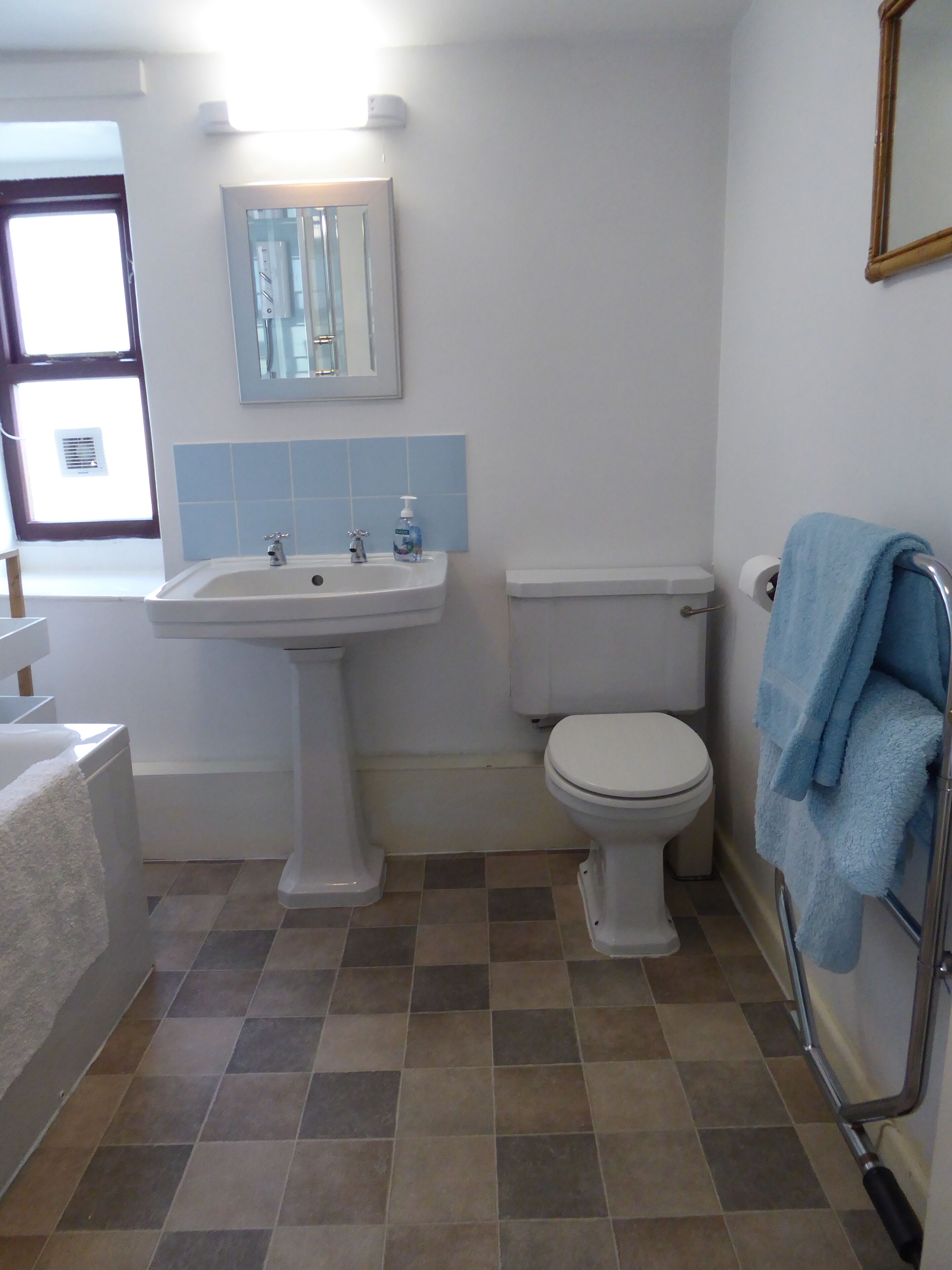 A bathroom with a pedestal sink, a toilet, and a towel rack with a blue towel.
