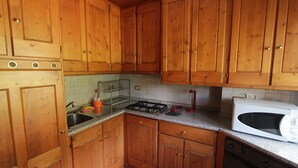 A kitchen with wooden cabinets, a gas stove, a microwave, and a sink. - Two steps from Cortina d'Ampezzo (Vodo)