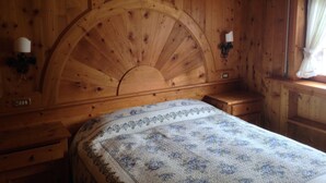 A wooden cabin-style room with a large bed, wooden walls, a curved headboard, and a window with curtains. - Two steps from Cortina d'Ampezzo (Vodo)