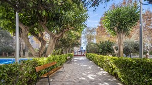 A paved walkway lined with benches and trees, leading to a building with a blue sign. - Edimar 2-3 (Benidorm)