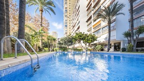 A swimming pool with metal railings, surrounded by palm trees and a multi-story building with balconies. - Edimar 2-3 (Benidorm)
