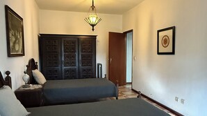Een slaapkamer met twee bedden, een kledingkast, een plafondventilator en een deur naar een andere kamer.