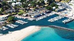 An aerial view of a coastal marina with boats docked, a sandy beach, and a breakwater structure.