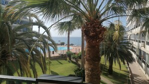 A balcony with a view of a swimming pool, palm trees, and a building with balconies.