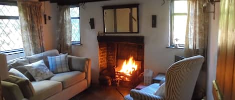 Ein gemütliches Wohnzimmer mit Kamin, einer Couch, einem gestreiften Ohrensessel und einem Fenster mit Vorhängen.