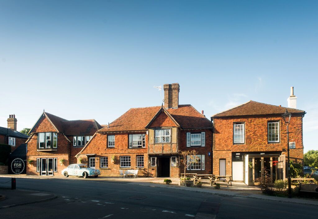 Un bâtiment traditionnel en briques, avec une entrée centrale, une voiture garée devant et une enseigne sur le côté gauche.