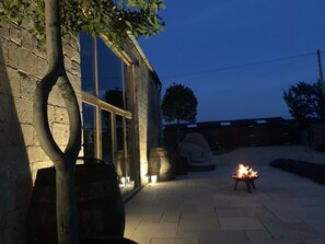 A stone building with large windows, a fire pit, and a tree in the foreground. - Unique converted Dovecote Grade II listed  sleeps 6 set in the Cotswolds. (Chipping Campden)