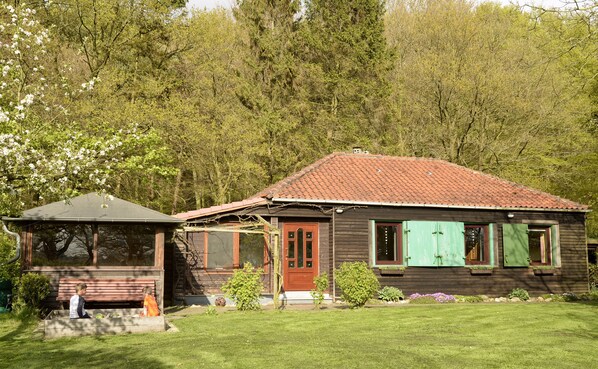 Une maison en bois avec un toit recouvert de tuiles rouges, une véranda en bois et un petit jardin.