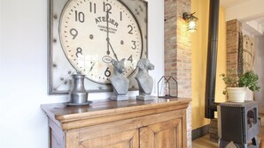 A vintage clock with a rustic wooden cabinet below it, a metal vase, and two dog sculptures on the cabinet.