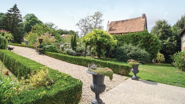 A well-maintained garden with a gravel path, neatly trimmed hedges, and two large urns with plants.