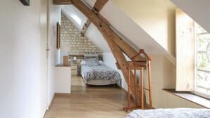 A bedroom with a sloped ceiling, a wooden ladder, a bed, a desk, and a window.