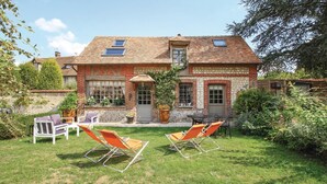 A two-story house with a brick exterior, a tiled roof, and a small garden with lawn chairs and a table.