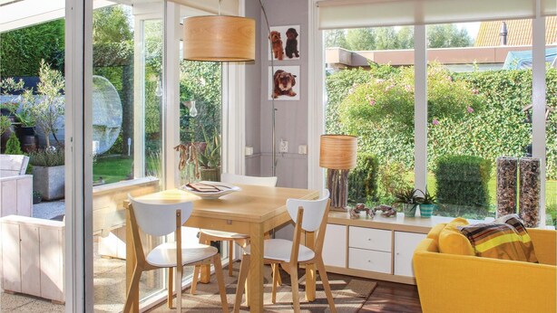 A bright kitchen with large windows, wooden furniture, and a view of a garden.