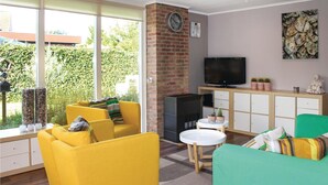 A bright living room with yellow sofas, a fireplace, a TV, and a view of greenery outside.