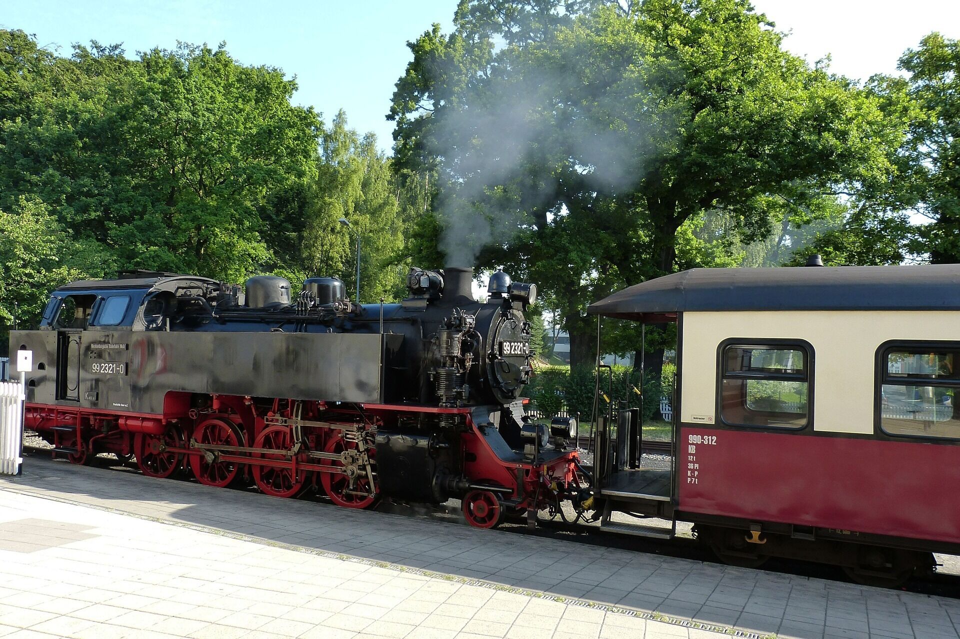 A steam locomotive with a red and black carriages at a station.