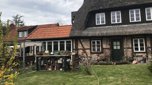 A traditional building with a thatched roof and a wooden facade, featuring large windows and a well-maintained lawn. - Charming suite with pool-sauna area, spa-wellness area, restaurant. (Börgerende-Rethwisch)