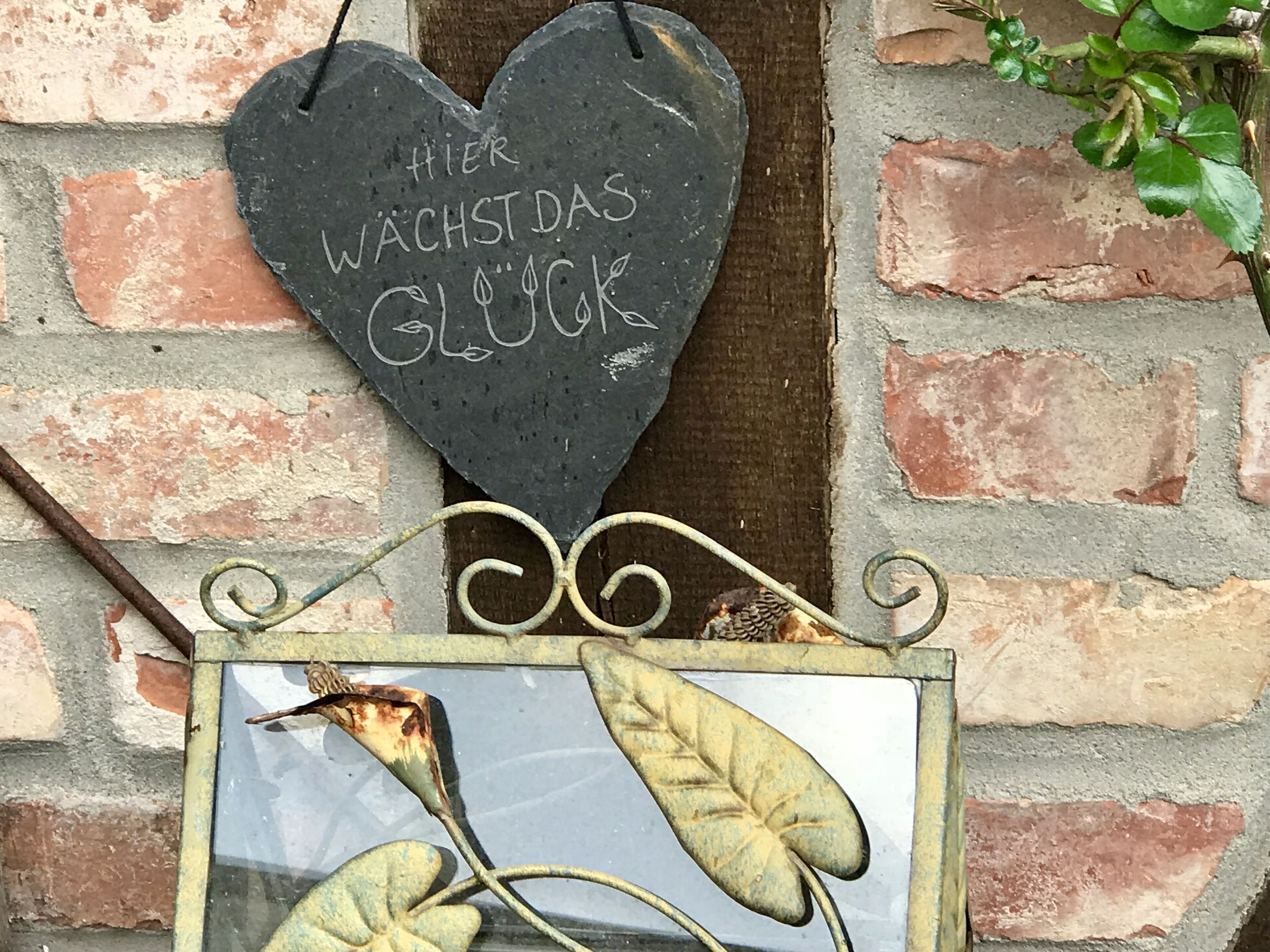 Un panneau en forme de cœur, portant un texte dans une langue étrangère, fixé à un mur de briques.